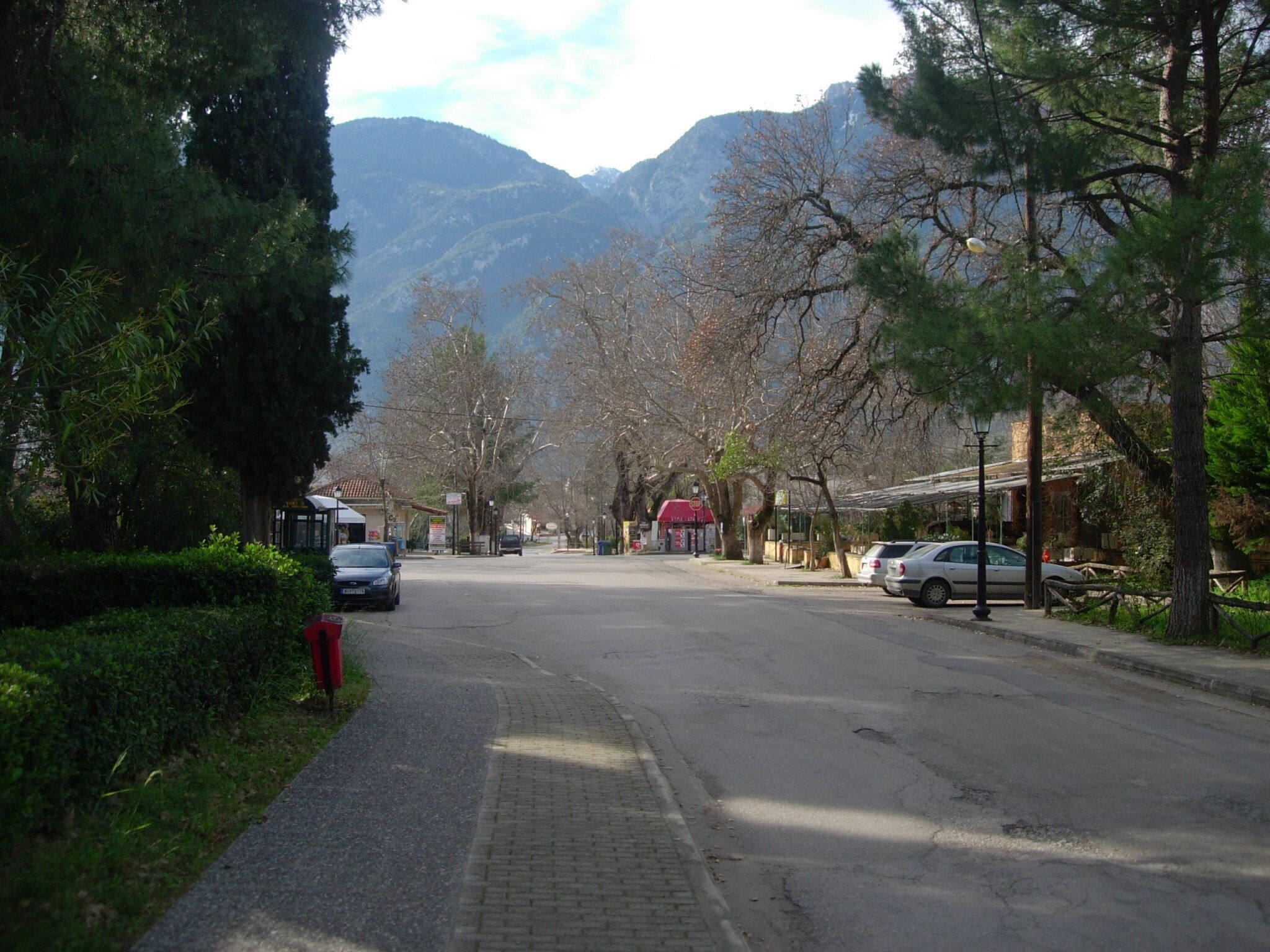 A street with parked cars, a sidewalk, and buildings with a mountain backdrop.