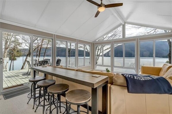A covered outdoor dining area with a bar, stools, and a view of a lake.