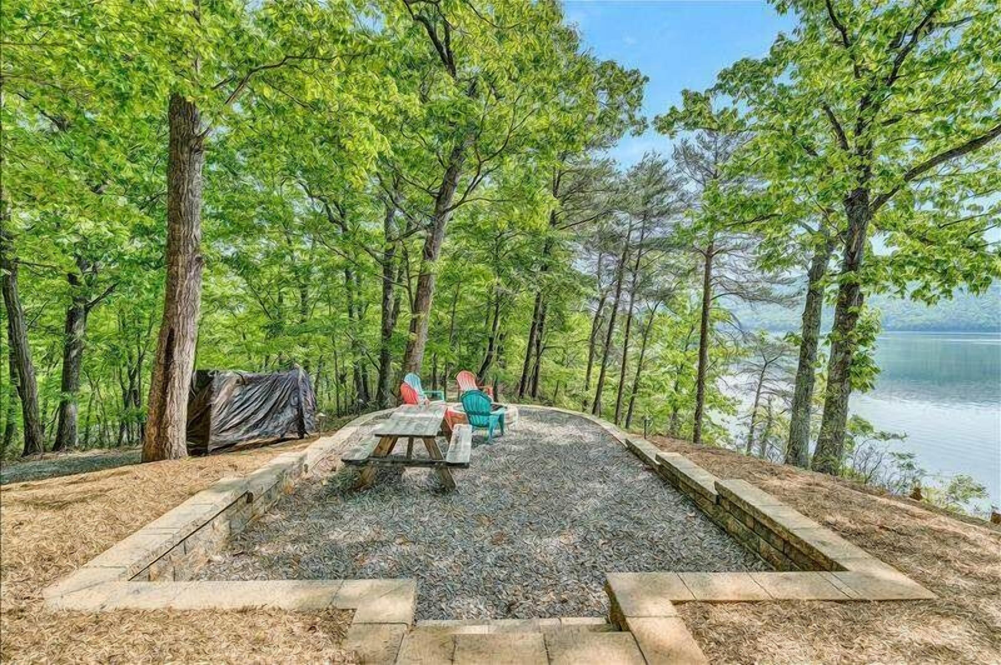 A picnic area with a table and chairs surrounded by trees, overlooking a body of water.