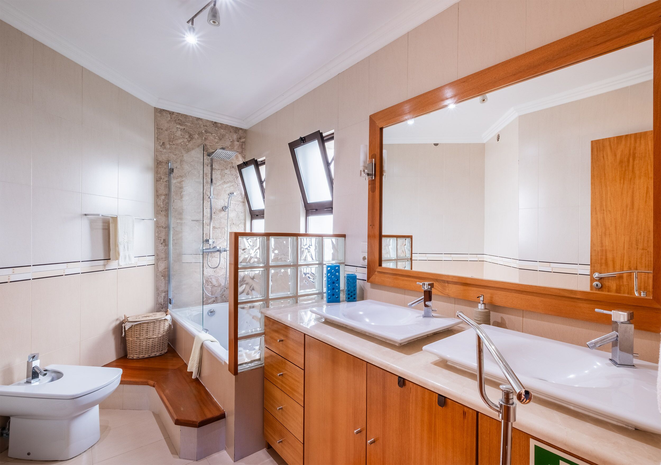 Een moderne badkamer met een douchecabine van glas, een grote spiegel en een houten wastafelmeubel met twee wasbakken.
