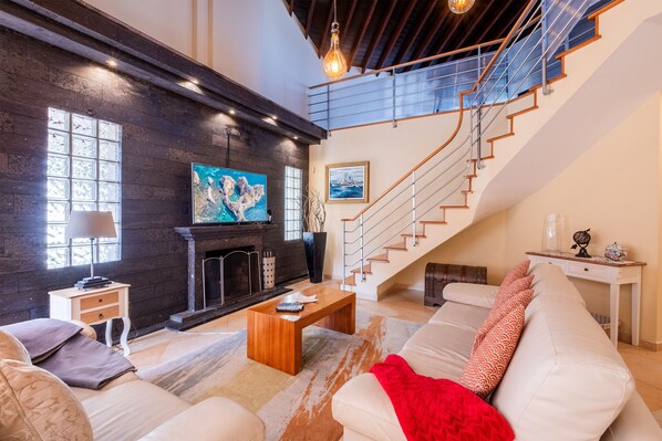 A spacious living room with a fireplace, a large TV, and a staircase leading to an upper level.