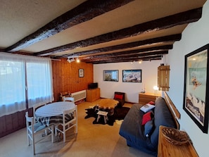 A cozy room with a wooden ceiling, a dining table with chairs, a sofa, and a TV. - Family apartment at the foot of the slopes (Saint-Lary-Soulan)