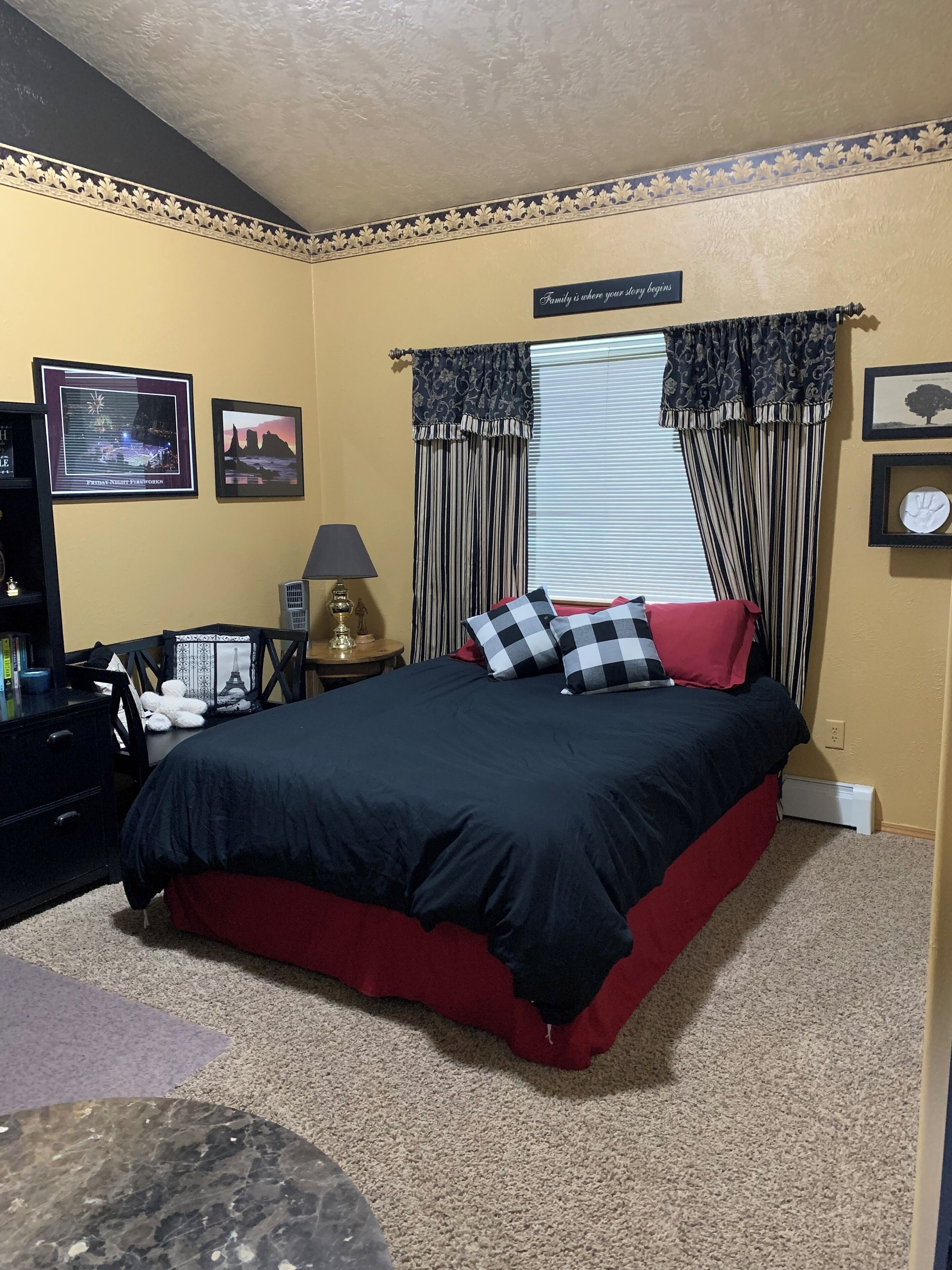 A bedroom with a large bed, a nightstand, a lamp, and a window with curtains.
