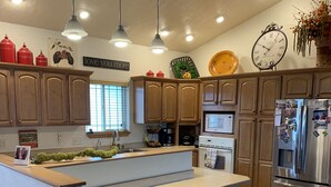 A modern kitchen with wooden cabinets, a central island with stools, stainless steel appliances, pendant lighting, and a clock on the wall. - Creekside Tranquility • Peaceful, Spacious Montana Home Near Missoula -20 Min (Florence)
