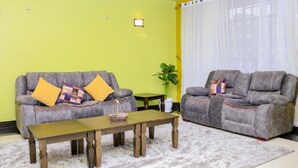 A living room with two grey sofas, a wooden coffee table, and a white shag rug. - Delight Mainstay Homes by Della (Nairobi)
