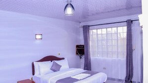 A bedroom with a bed, a bedside table, a wall-mounted TV, and a window with curtains. - Delight Mainstay Homes by Della (Nairobi)