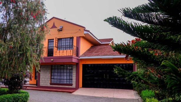 A two-story house with a red-tiled roof, a balcony, and a garage. - Delight Mainstay Homes by Della (Nairobi)