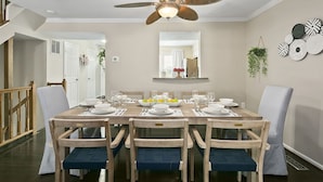 A dining room with a wooden table set for six, surrounded by chairs with blue cushions. A ceiling fan with a light fixture is above the table. - Finchwood: Private Yard & Near DC (Sterling)
