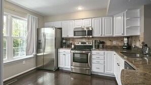 A modern kitchen with white cabinetry, stainless steel appliances, a granite countertop, and a window with curtains. - Finchwood: Private Yard & Near DC (Sterling)