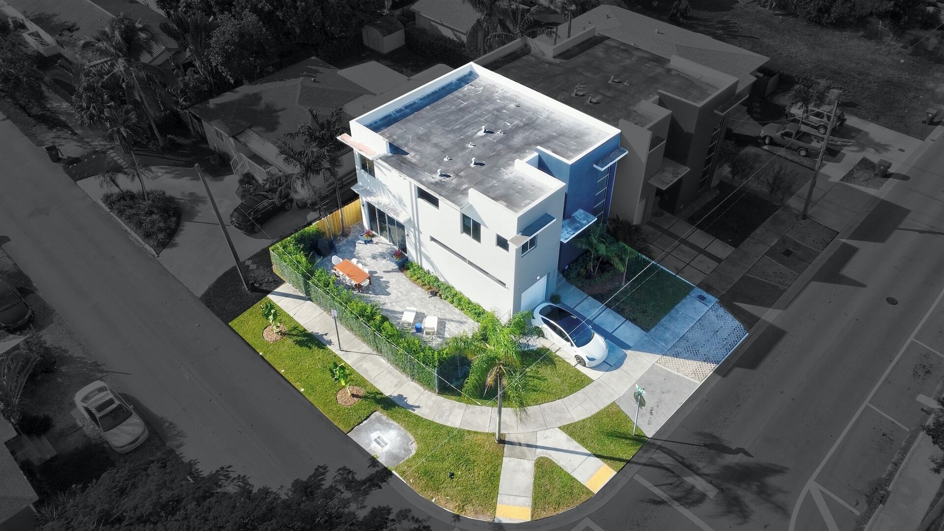 An aerial view of a modern two-story house with a flat roof, a small front yard, and a driveway.