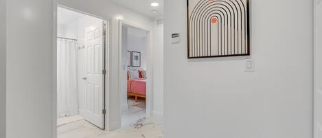 Um corredor com paredes brancas, chão de mármore e uma obra de arte abstrata emoldurada.
