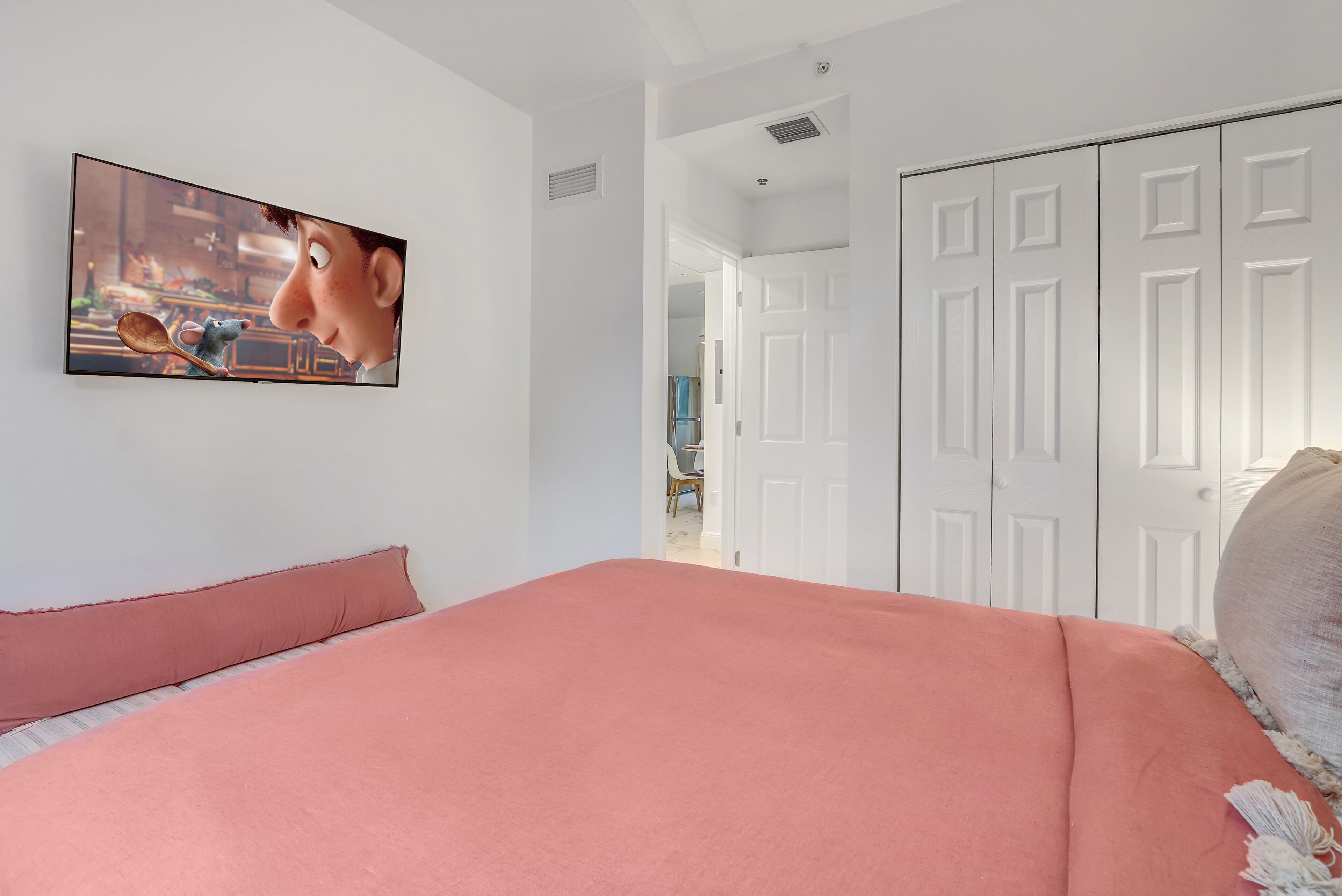 Un dormitorio con una cama grande, un televisor instalado en la pared y un armario.