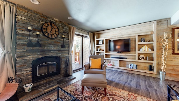 Una sala de estar acogedora con chimenea de piedra, un sillón cómodo, un televisor de pantalla plana, estanterías de madera y un reloj grande.