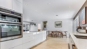 Une cuisine moderne dotée d’appareils électroménagers intégrés, un coin repas avec une table et des chaises, et une vue sur l’extérieur.