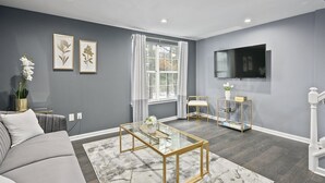 Un soggiorno moderno con un divano grigio, un tavolino in vetro e una TV a parete.