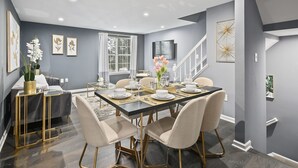 Una sala da pranzo moderna con un tavolo in legno scuro apparecchiato per sei persone, circondato da sedie beige rivestite con gambe dorate.
