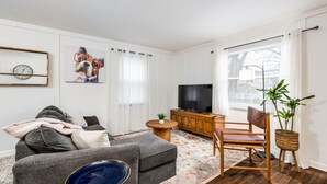 A living room with a grey sofa, a wooden cabinet, a television, and a plant. - City Boho ✦ New Kitchen ✦ King Bed (Bexley)