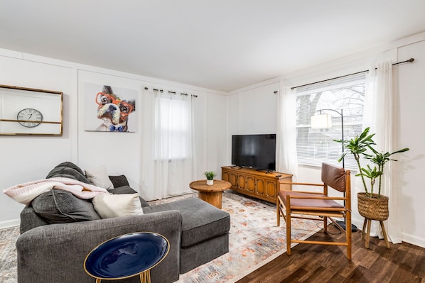 Ein Wohnzimmer mit grauem Sofa, einem Holzschrank, einem Fernseher und einer Pflanze.
