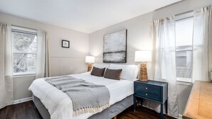 A bedroom with a large bed, two bedside tables, a nightstand, and a painting on the wall. - City Boho ✦ New Kitchen ✦ King Bed (Bexley)