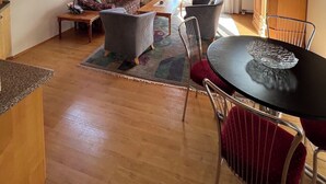 Ein gemütliches Wohnzimmer mit Holzbalkendecke, einer Couch, einem Couchtisch und einem Esstisch mit Stühlen.