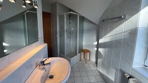 Ein modernes Badezimmer mit einem großen Spiegel, einem Waschbecken, einer Dusche und einem kleinen Hocker.