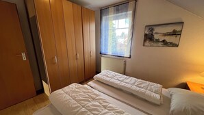 Ein Schlafzimmer mit zwei Einzelbetten, einem Holzschrank, einem Fenster mit Ausblick und einem Bild an der Wand.