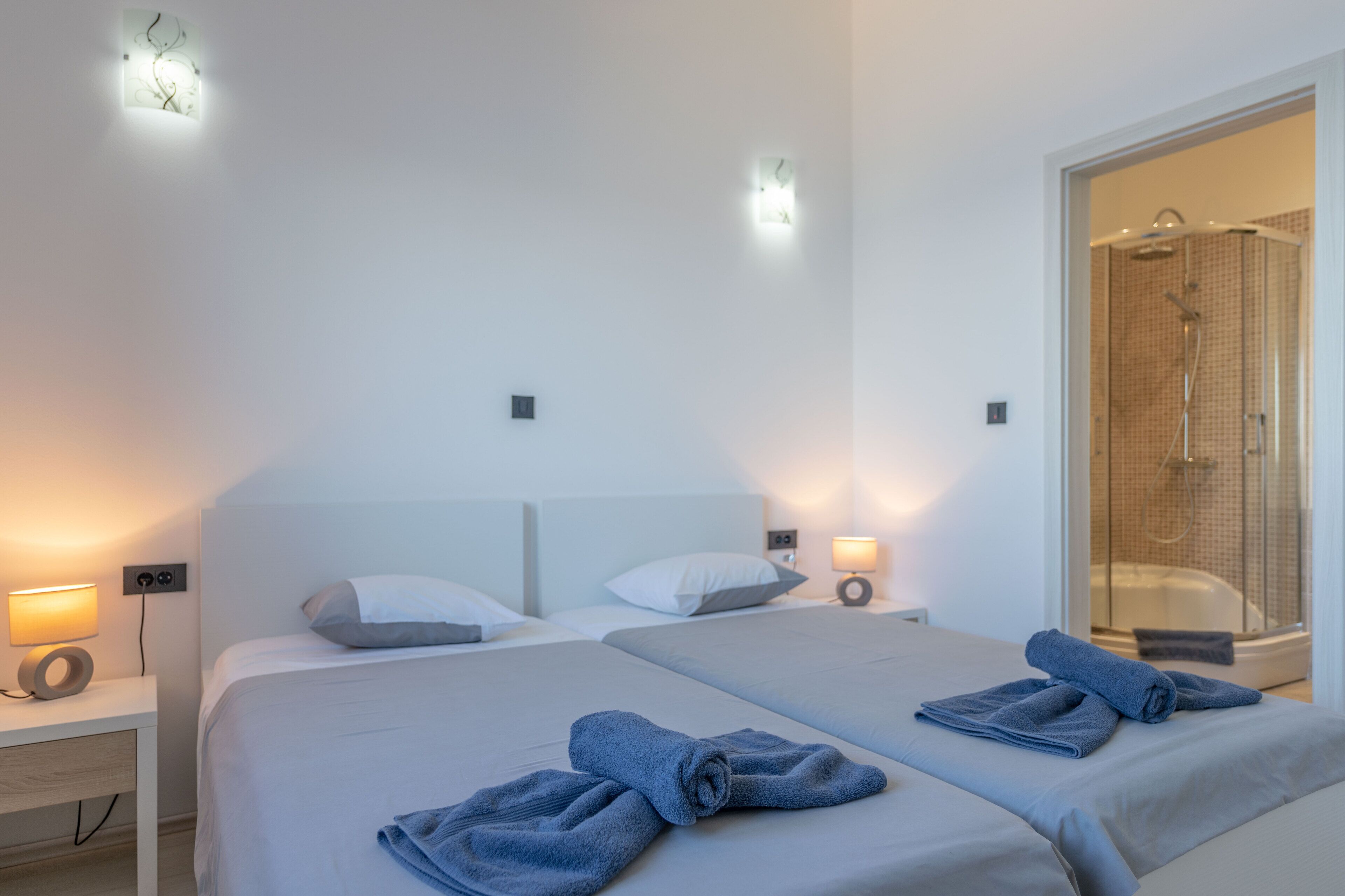 A hotel room with two beds, a shower area, and wall-mounted lights.
