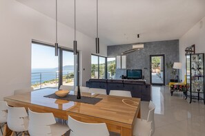 A modern dining area with a glass table, white chairs, and a view of the sea. - A magical view of the sea, a magical villa (Labin)