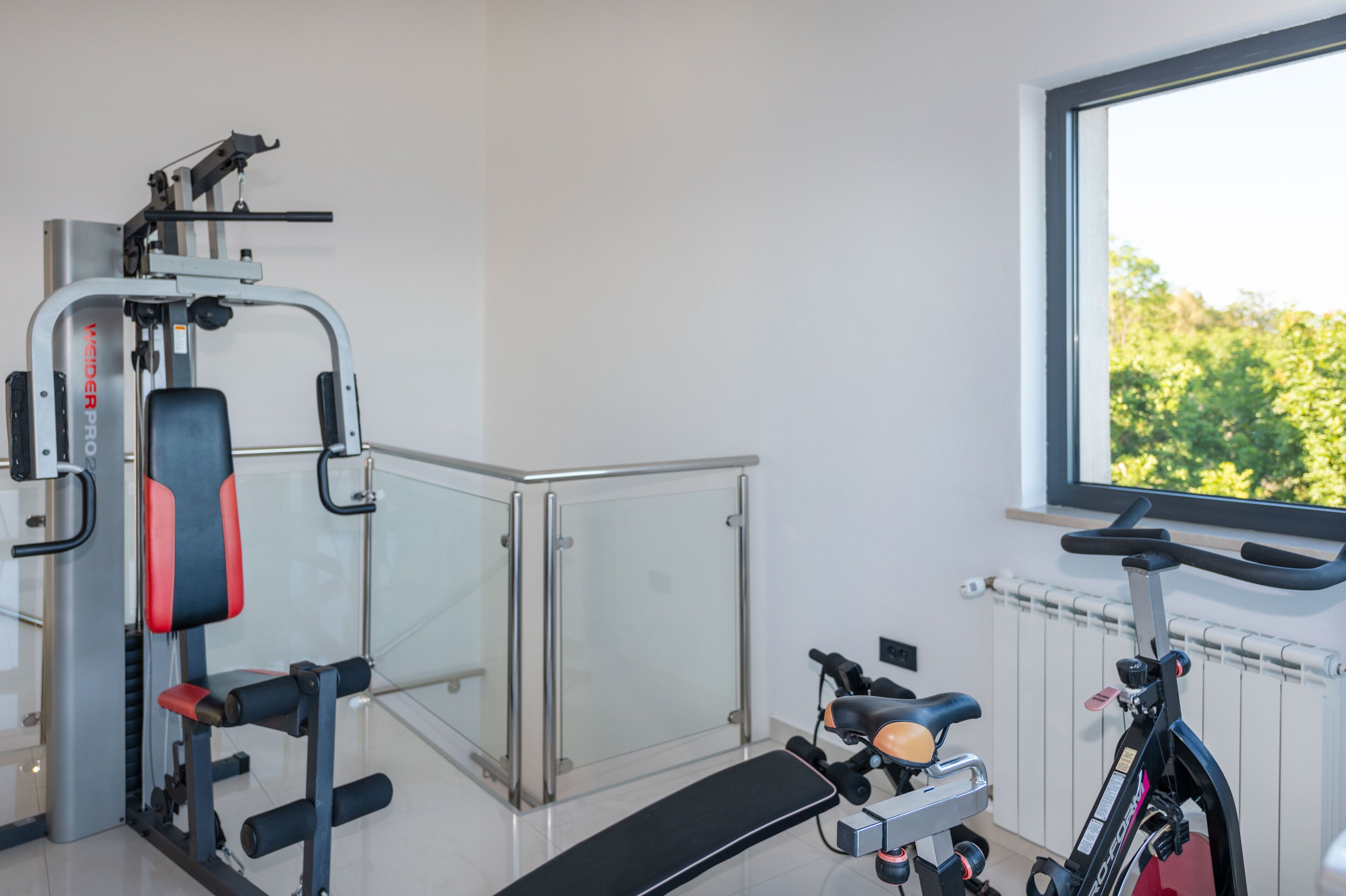 A gym with exercise equipment, a bench, and a window with a view of greenery.