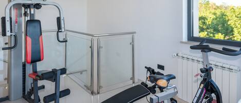 A gym with exercise equipment, a bench, and a window with a view of greenery.