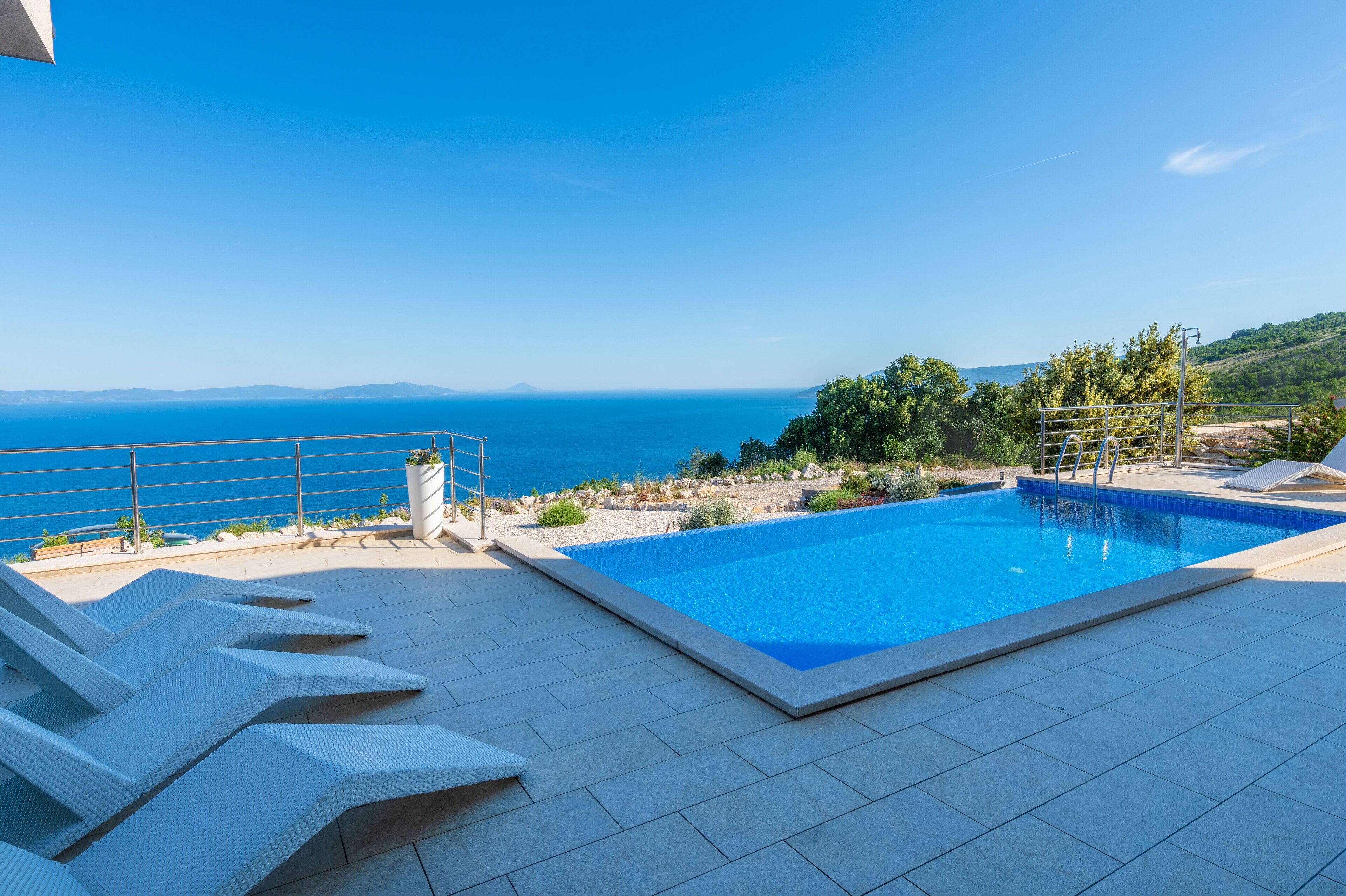 A rectangular swimming pool with a clear blue sky and distant mountains in the background.