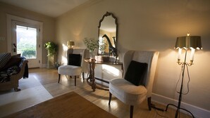 Una sala de estar con piso de madera, dos sillones, una mesa, un espejo y una lámpara de pie.