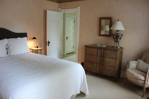 A bedroom with a bed, a dresser, a chair, and a nightstand with a lamp.