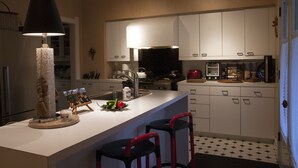 Una cocina moderna con armarios blancos, una isla central con taburetes, una lámpara de araña y un suelo de baldosas blanco y negro.