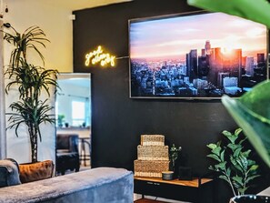 A modern living room with a cityscape TV, a neon sign, and a stack of woven baskets.
