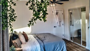 Un dormitorio con cama, ventilador de techo, una puerta con una toalla colgada y una puerta corrediza de vidrio.
