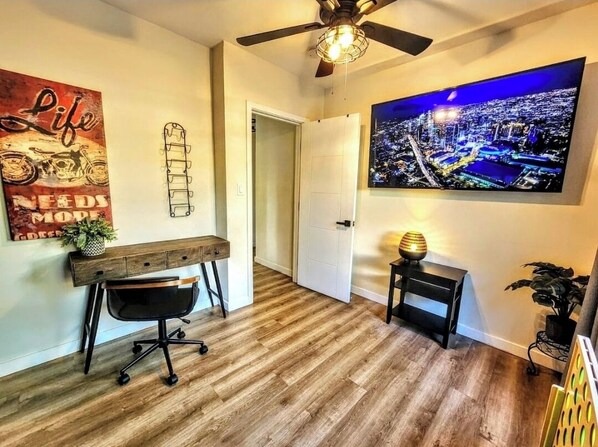 A modern home office with a wooden desk, office chair, and a cityscape painting.