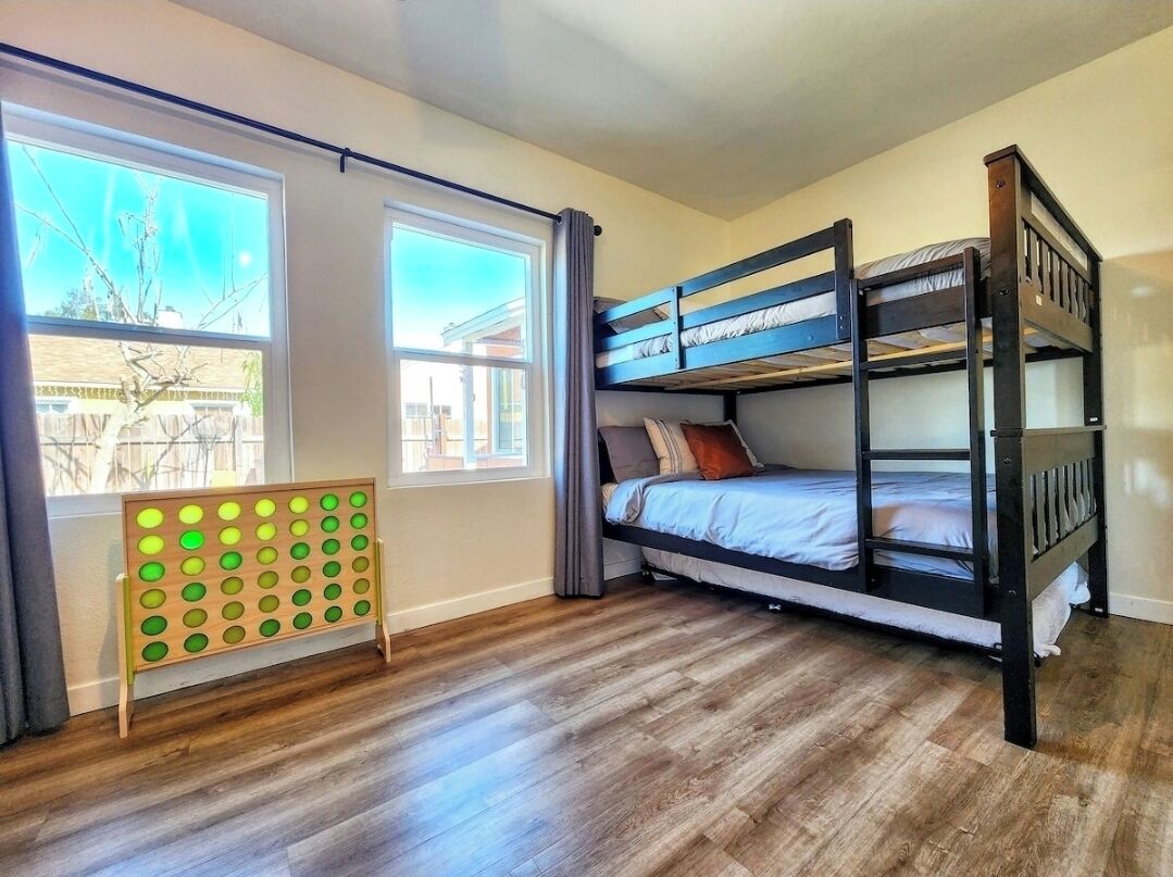 Une chambre avec des lits superposés donnant sur un quartier résidentiel, un plancher en bois et un panneau perforé avec des trous circulaires.