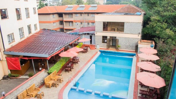 A swimming pool with lounge chairs and umbrellas, surrounded by buildings with red roofs and a brick facade. - Delight Homes by Della (Nairobi)