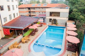 Uma piscina com espreguiçadeiras e guarda-sóis, cercada por edifícios com telhados vermelhos e fachada de tijolos.