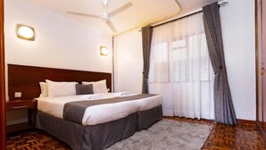 A neatly arranged bedroom with a bed, a nightstand, a ceiling fan, and a window with curtains. - Delight Homes by Della (Nairobi)