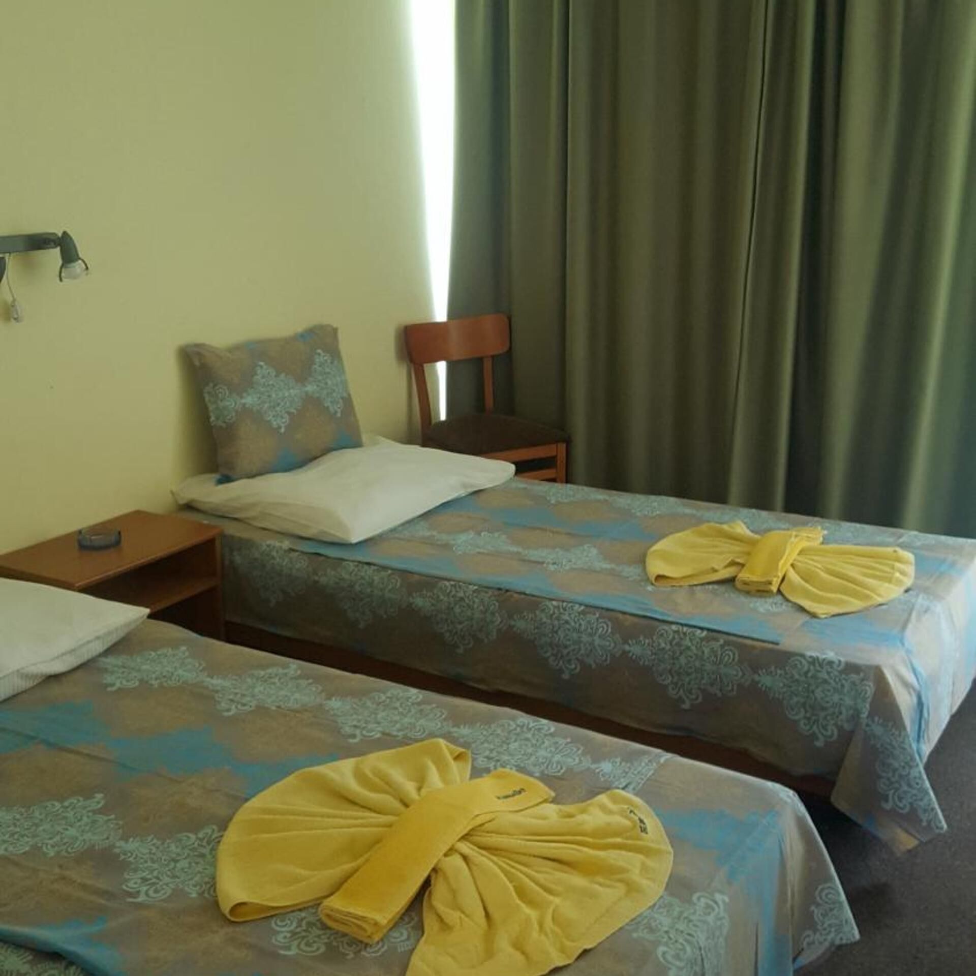 A hotel room with two beds, a nightstand, a chair, and a window with curtains.