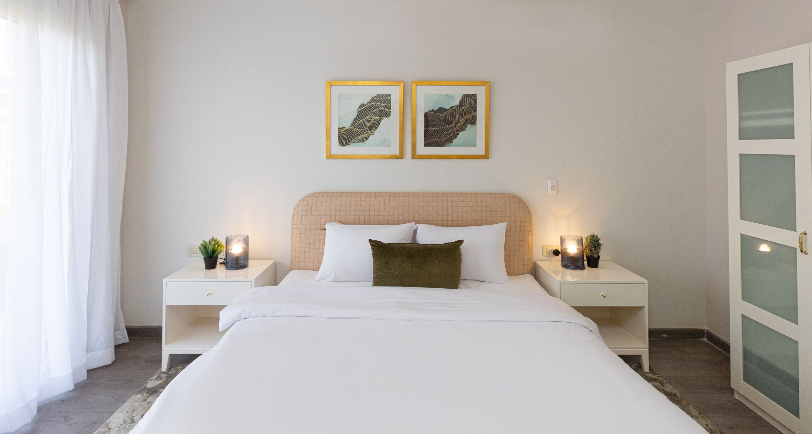 A neatly arranged bedroom with a bed, bedside tables, and two framed artworks on the wall.
