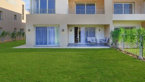 Un edificio residencial moderno de dos pisos con techo plano, ventanas amplias y un patio cubierto con mobiliario exterior.