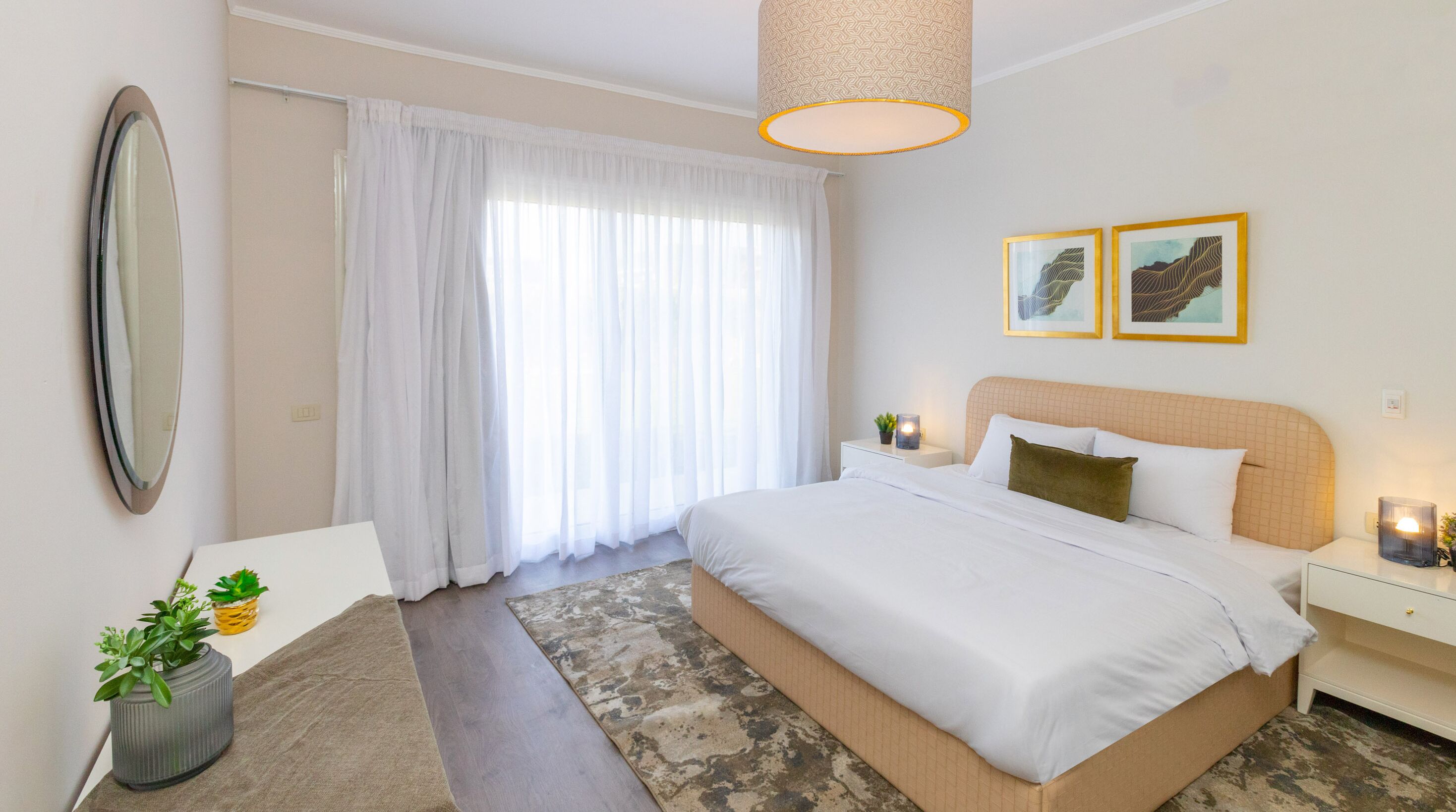 A hotel room with a large bed, a bedside table with a lamp, a mirror, and two framed pictures on the wall.