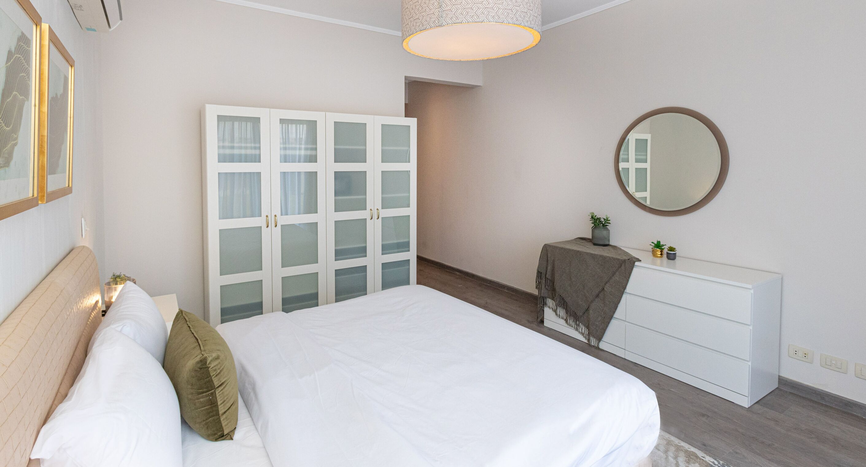 A bedroom with a bed, a wardrobe, a mirror, and a small table with a plant.