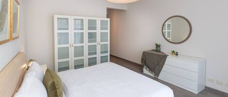 A bedroom with a bed, a wardrobe, a mirror, and a small table with a plant.