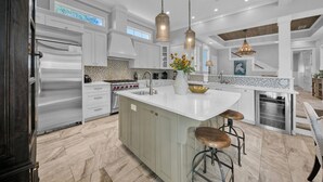 Una cocina amplia con una isla grande, electrodomésticos de acero inoxidable e iluminación colgante.