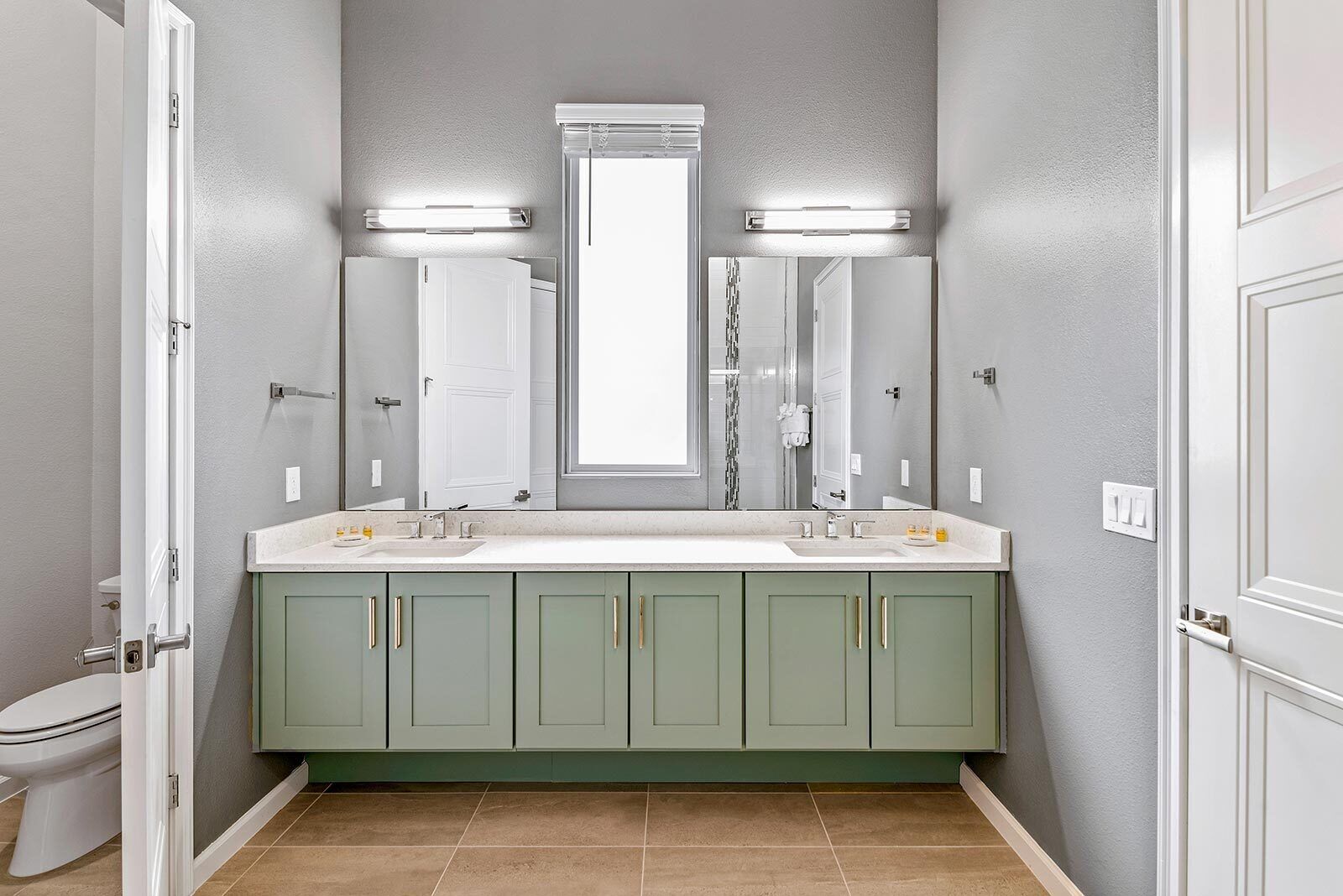 Une salle de bain avec un double lavabo, deux miroirs de coiffeuse et une fenêtre située au-dessus du miroir.