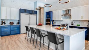 A modern kitchen with a central island, bar stools, and a stainless steel range hood. - Trendy Home w Trampoline RM, Bowling, Fantasy Themed BR & Theater - Near Disney (Davenport)